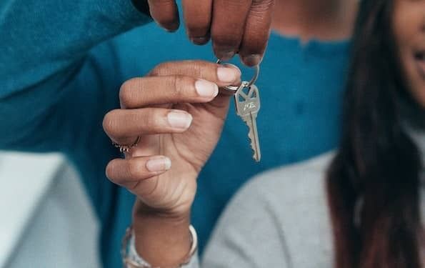 Photo of a man and woman holding the key to their new home. The man is wearing a blue long-sleeved shirt and the woman wears a light grey sweater.