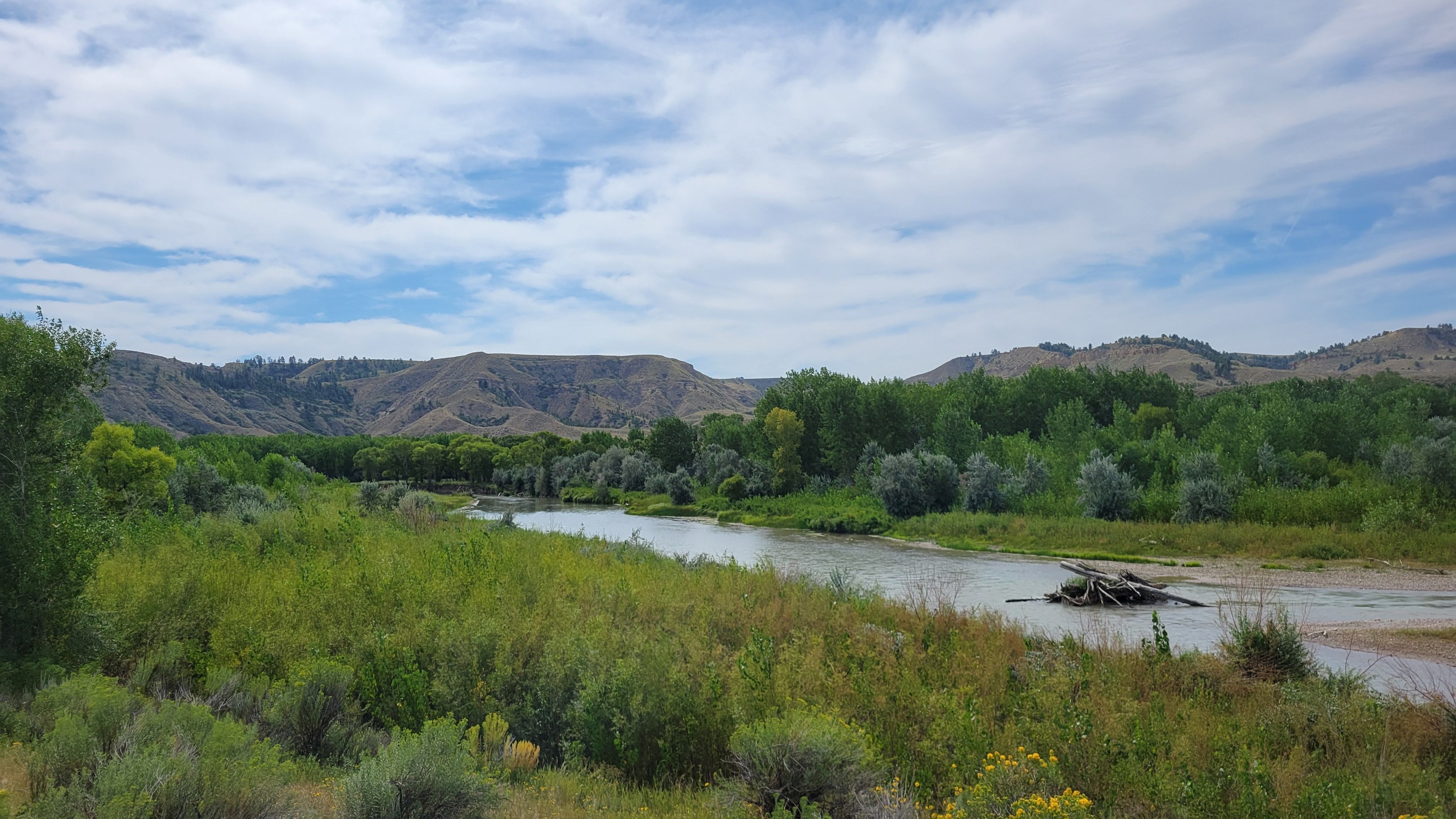 A view of a wide river among grassy plains and rolling brown hills.