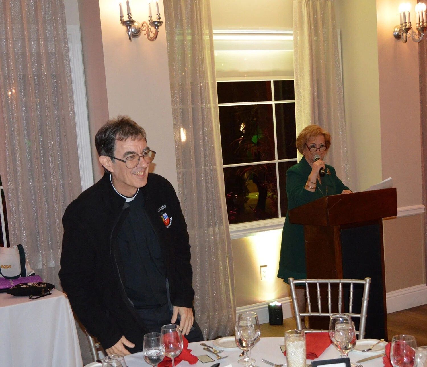Father Serge Dubé, parochial vicar at Holy Cross in Vero Beach, is introduced during the Serra Club dinner by Kathy Reese, right, Dec. 11, 2025.  WILLIAM CONE | FC