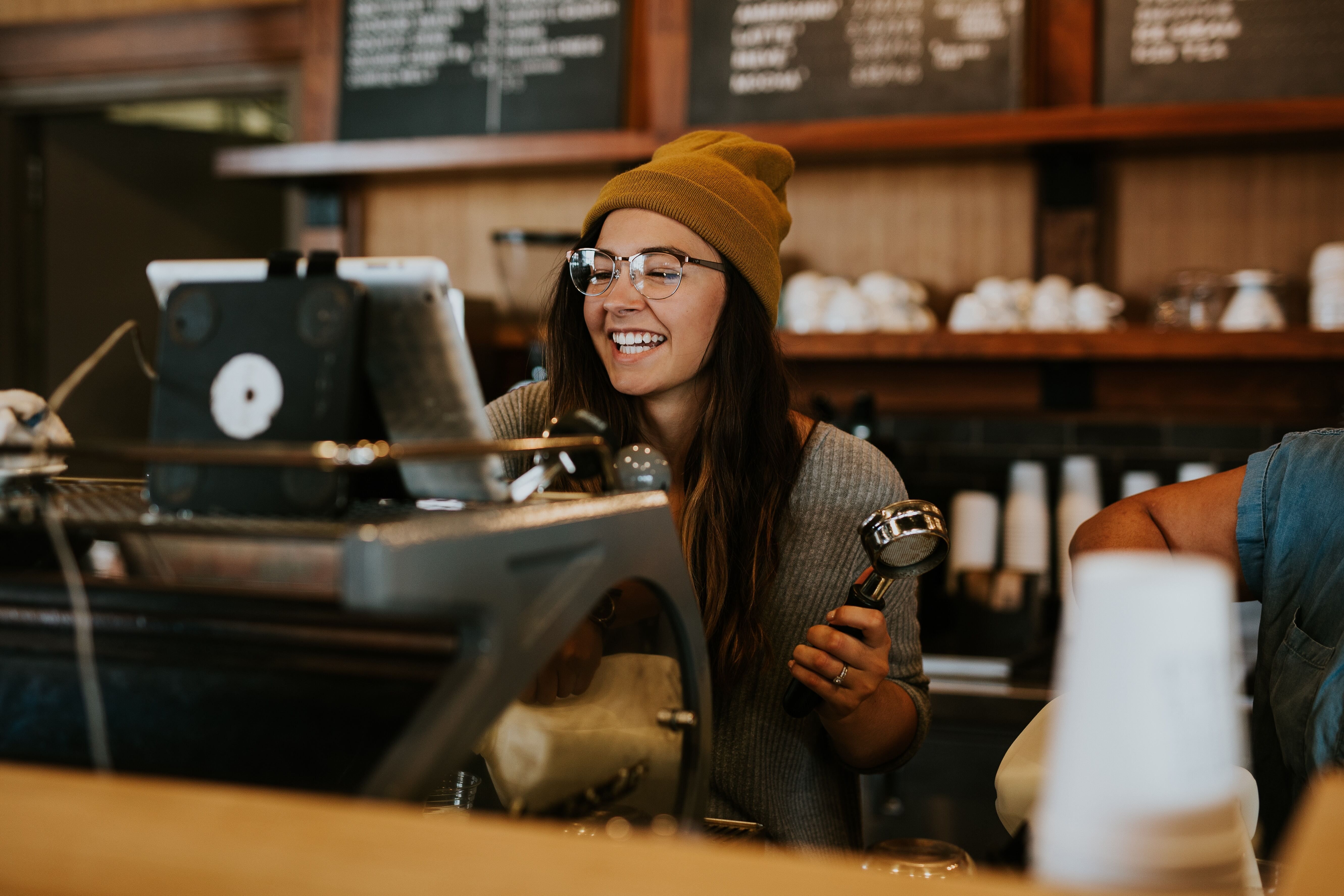 Young lady wearing glasses and a hat preparing someone's coffee order.