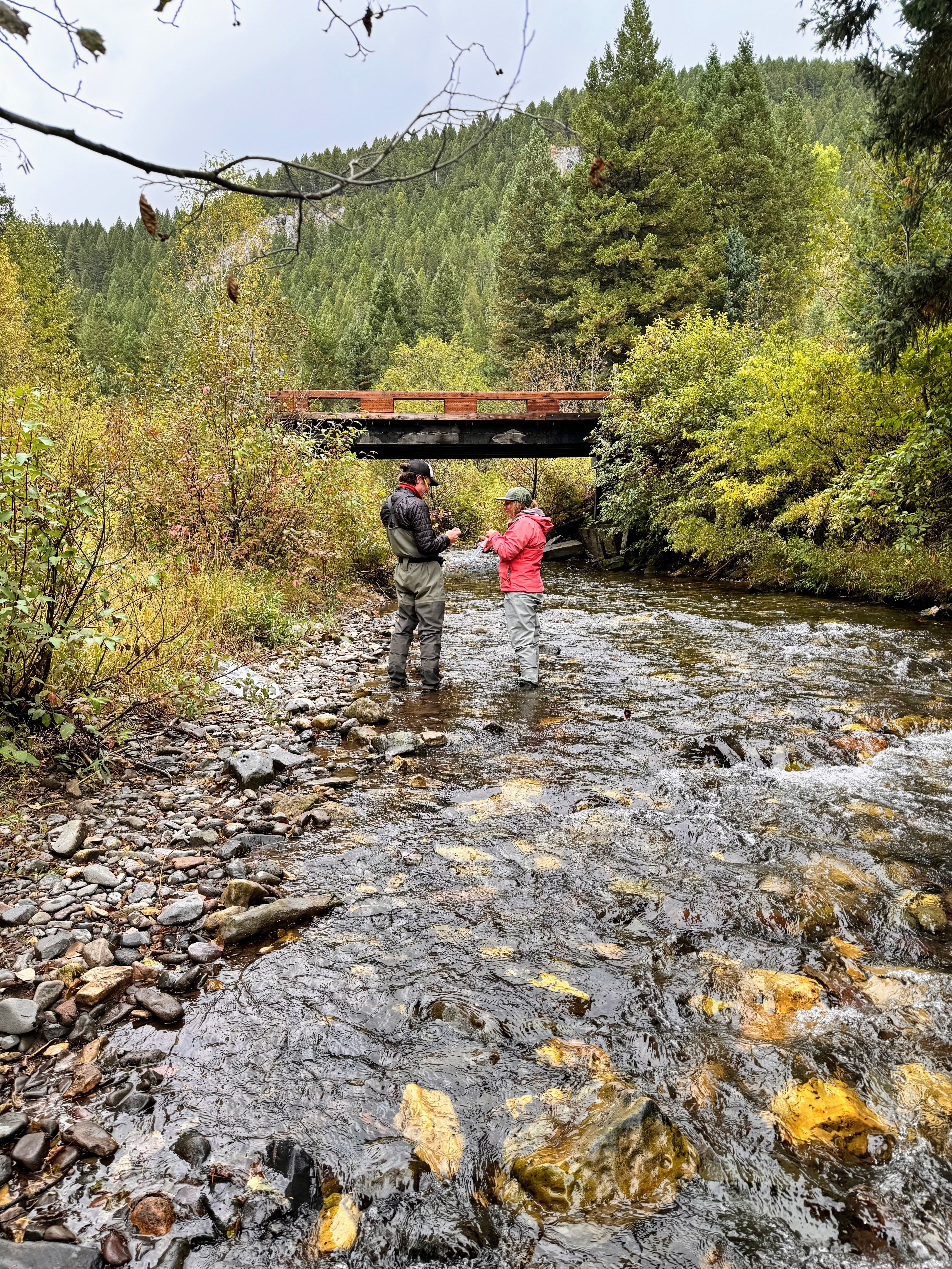 An MCC member and a project partner stand in a creek bed, making measurements.