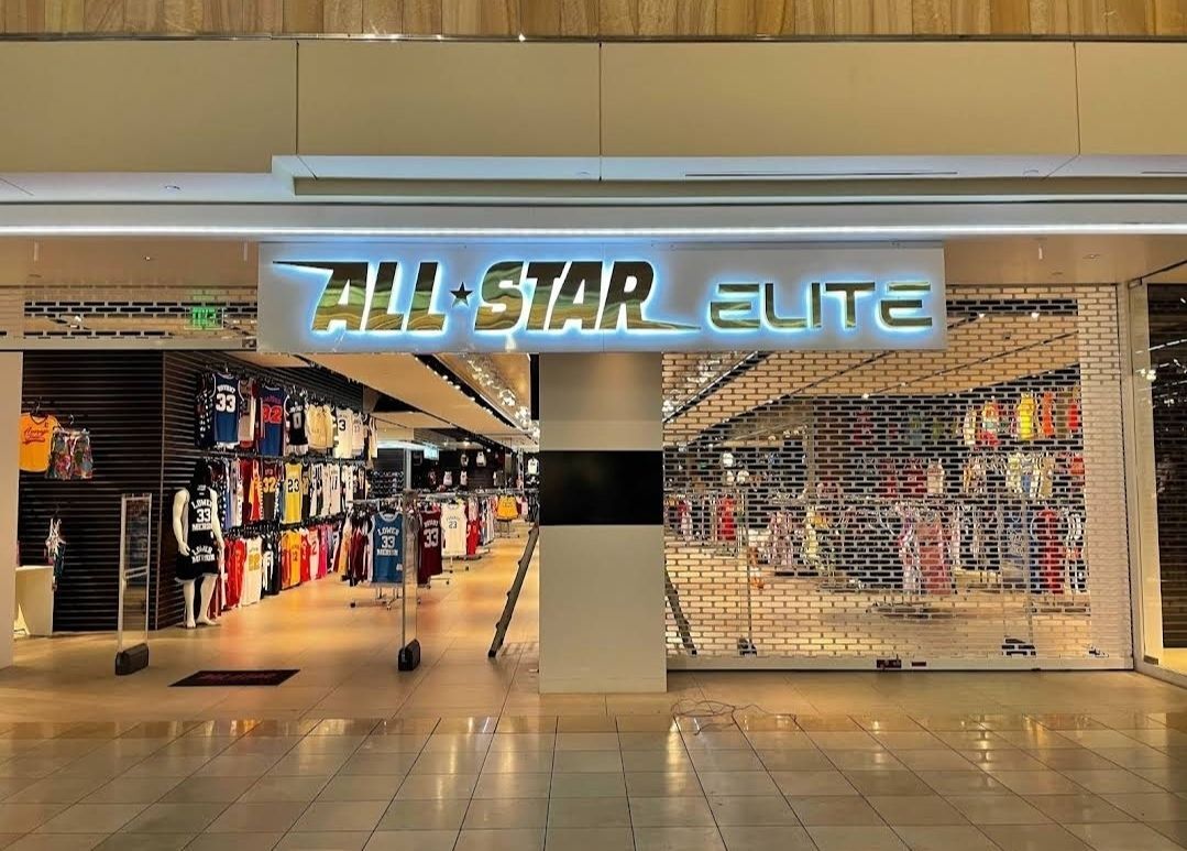 ibrant indoor LED sign displaying the All-Star Elite brand above the entrance of a sports apparel retail store in a shopping mall, featuring edge-lit halo glow for high visibility.