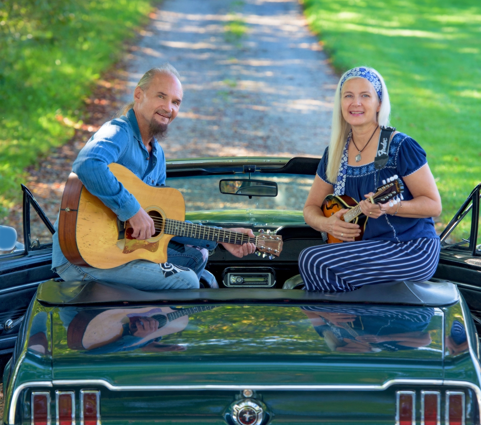 JD and Cindy holding instruments looking at the camera from the back of a Ford Mustang convertible