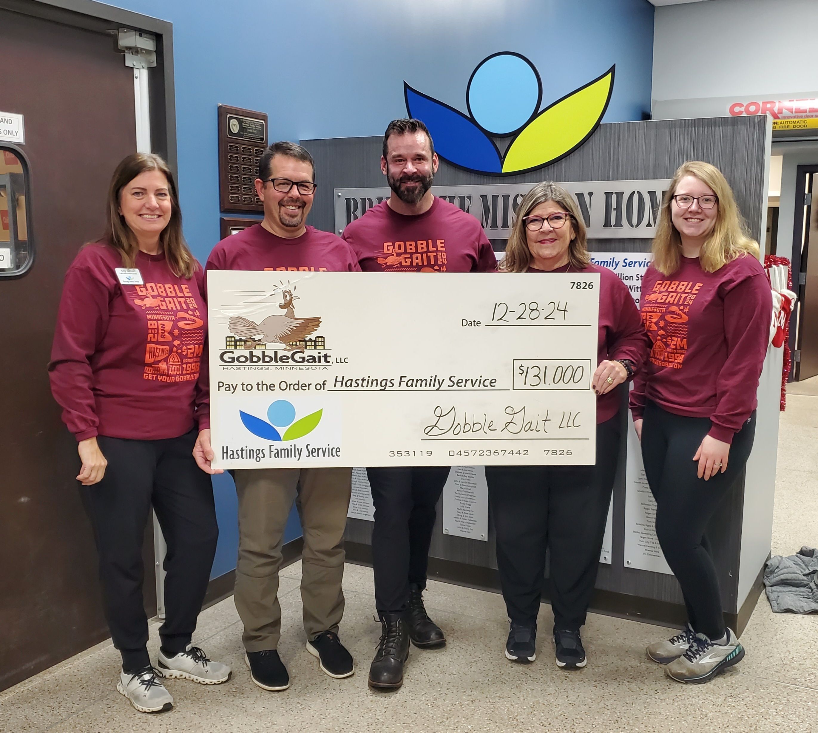 Group  of five dressed in Gobble Gait 2024 race shirts holding a larger check made out to Hastings Family Service for $131,000.