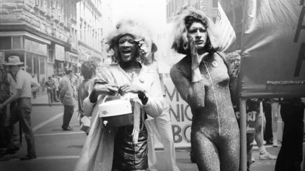 Marsha P. Johnson and Sylvia Rivera march down a street in New York City dressed in flamboyant streetwear. 