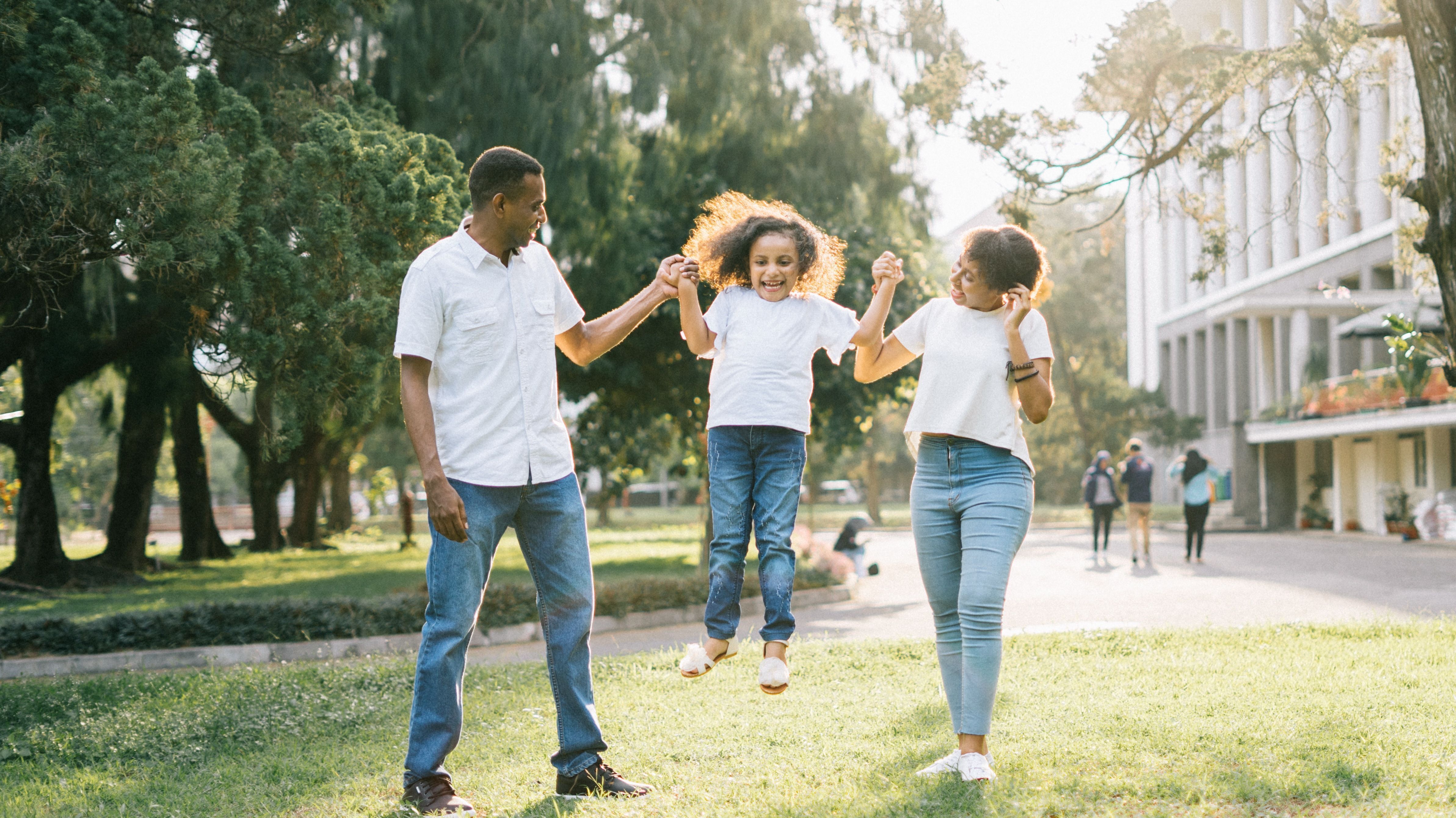 Parents hold hand with young child while walking outdoors on college campus