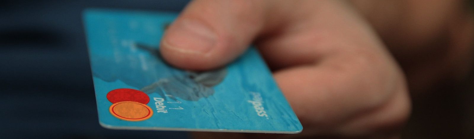 Closeup photo of a man's hand holding a light blue debit card with the MasterCard symbol on it.