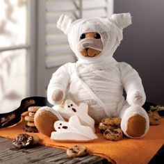 Stuffed teddy bear dressed as a mummy surrounded by ghosts and Halloween treats