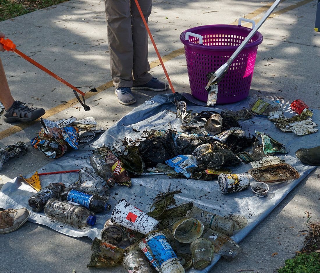 People using grabbers to collect litter onto a tarp, with a purple basket nearby.