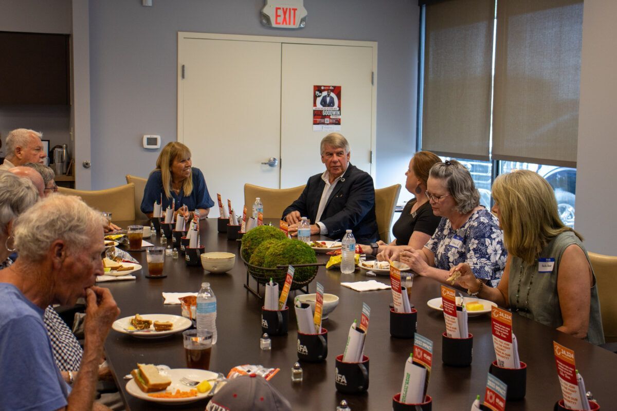 A group of people seated around a conference table with food, drinks, and informational materials.