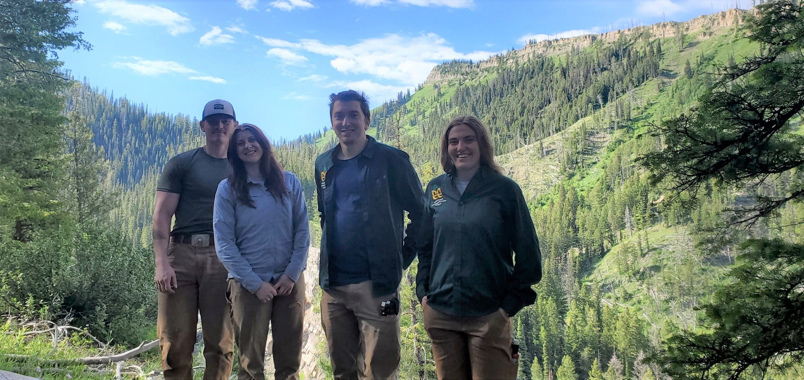 A crew stands smiling in front of an overlook to a forested hillside.