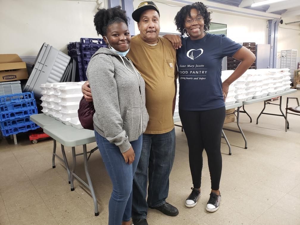 SM Josette Food Pantry staff smile at the camera in front of packages of food. 