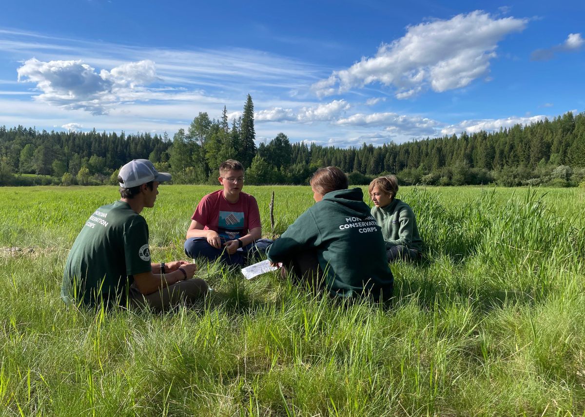 [Image description: A youth crew reads in a green meadow]