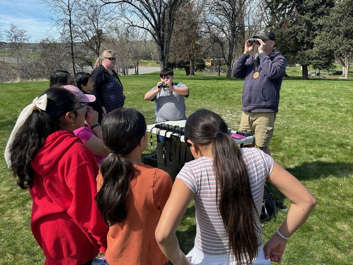 A volunteer demonstrates how to use binoculars to a group of students.