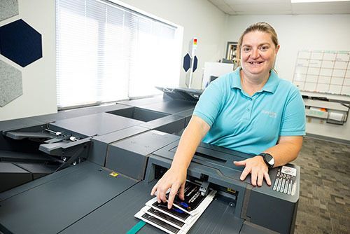 Woman standing at printer handling printed booklets