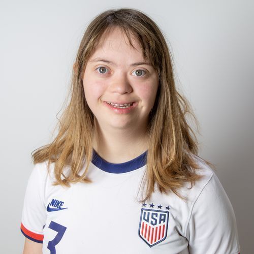 Sophia wears a white soccer jersey and smiles.