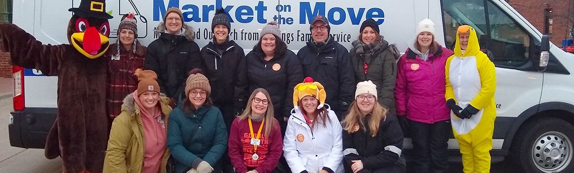 Group of HFS staff bundled up standing in front of the Market on the Move van at Gobble Gait 2024 with Mercy the Gobble Gait turkey.