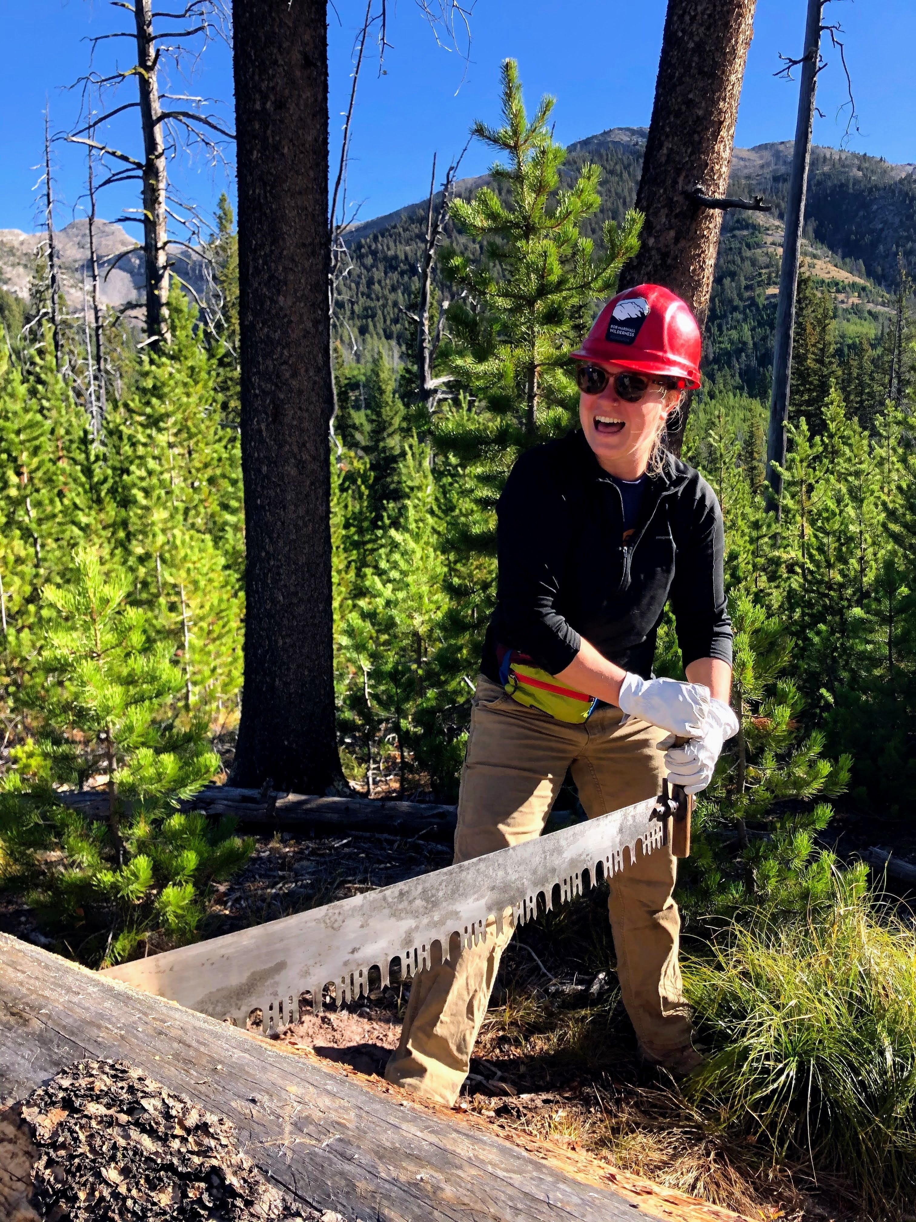 Allison uses a crosscut saw on a large log