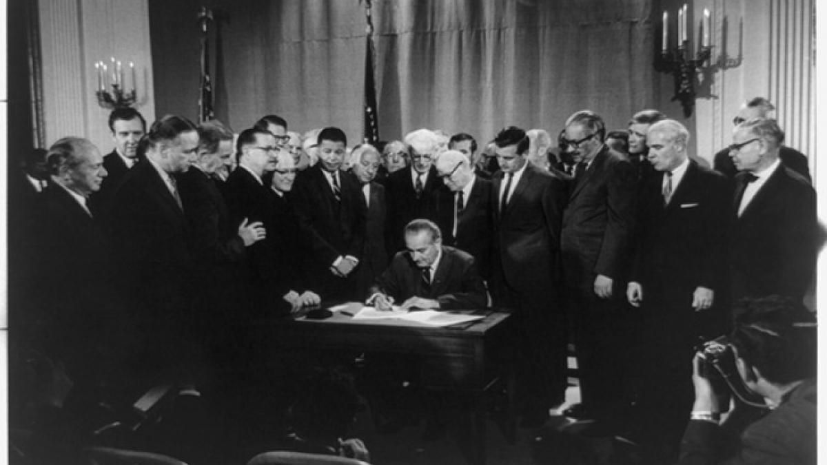 President Lyndon B. Johnson signs the Fair Housing Act on April 11, 1968, surrounded by members of Congress and civil rights advocates in the White House.