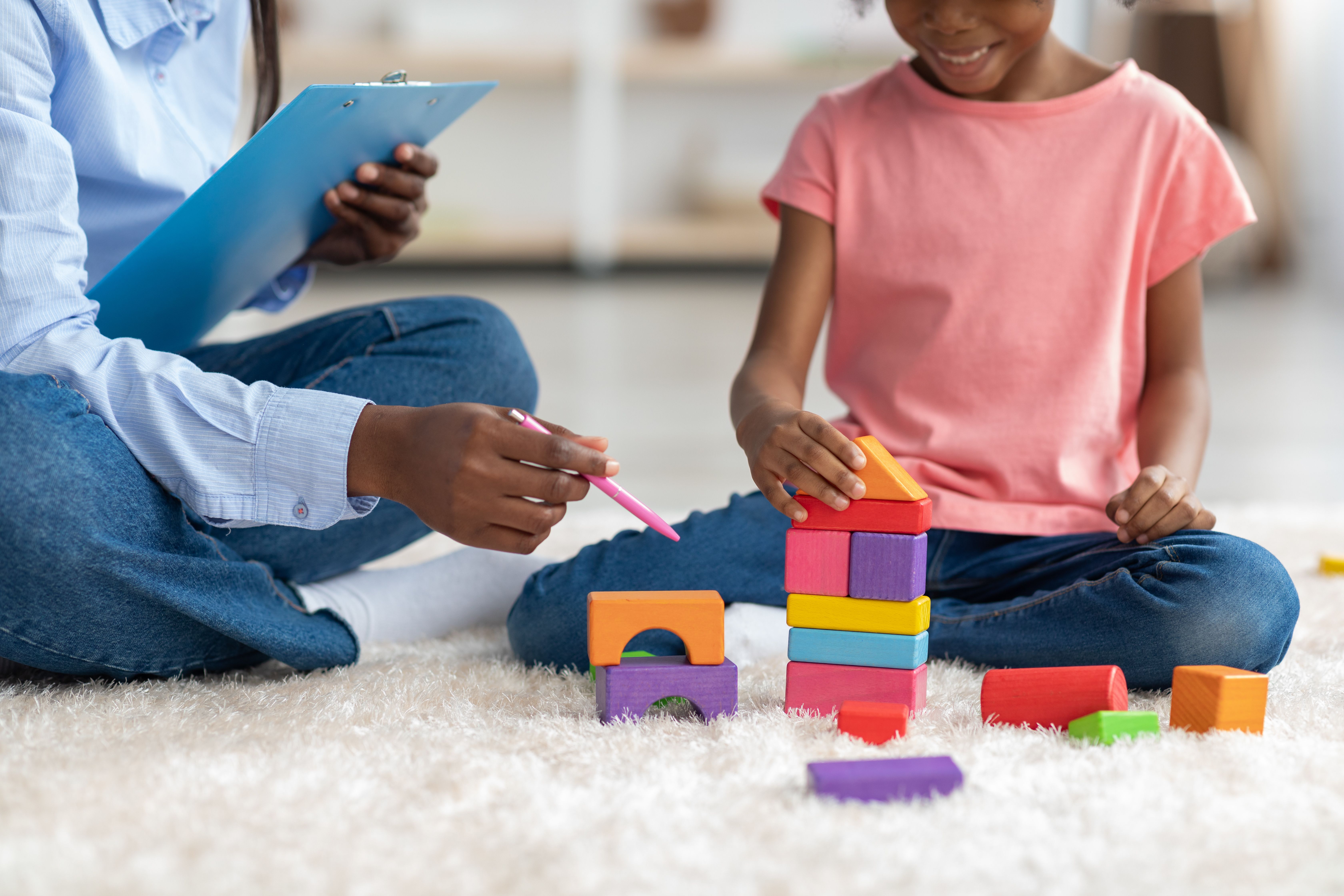 Image of a child playing with colorful blocks being observed by a woman.