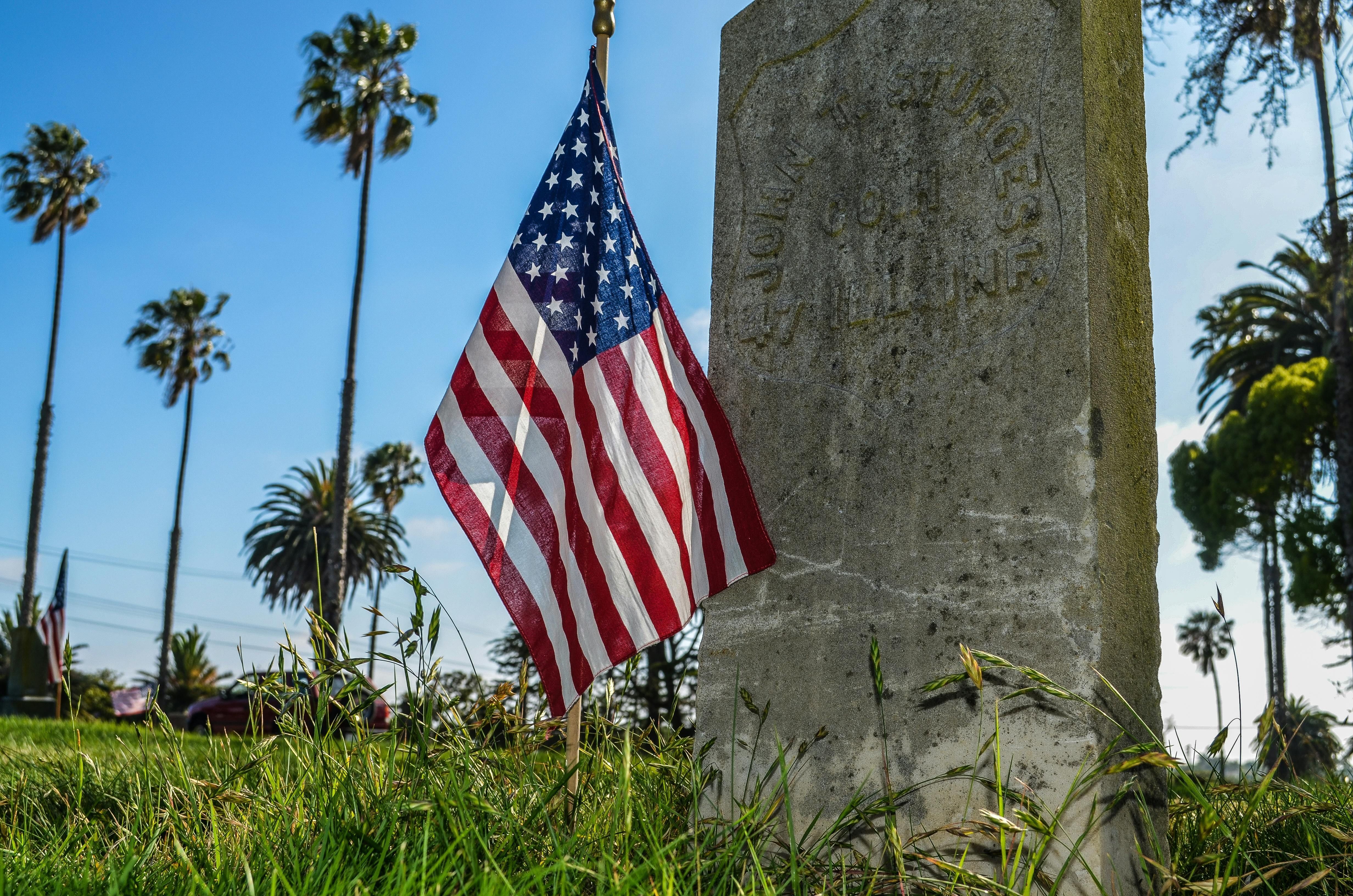 A small American flag stands next to a grave.