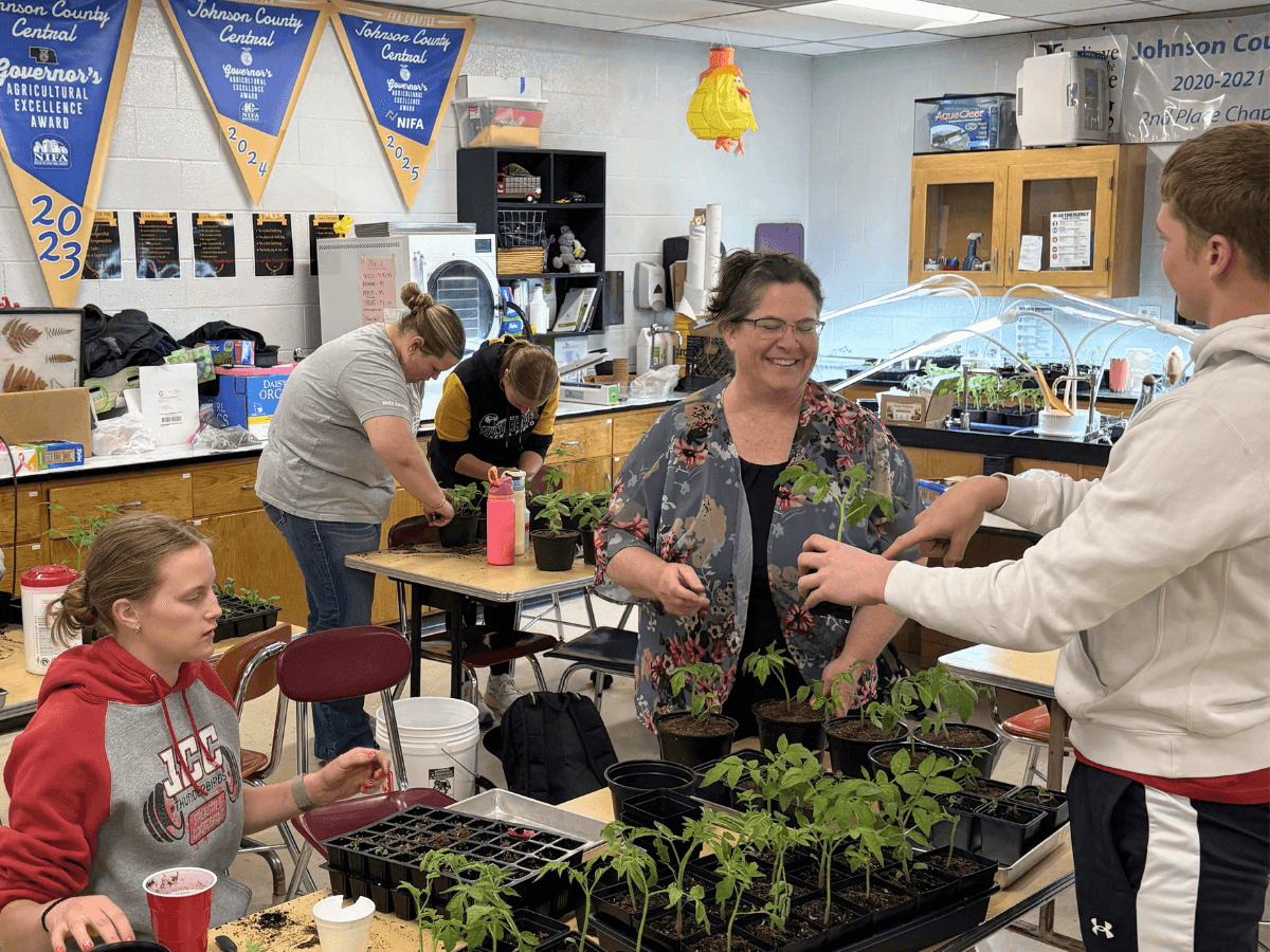 Teacher is helping students with plants in an agriculture classroom. 