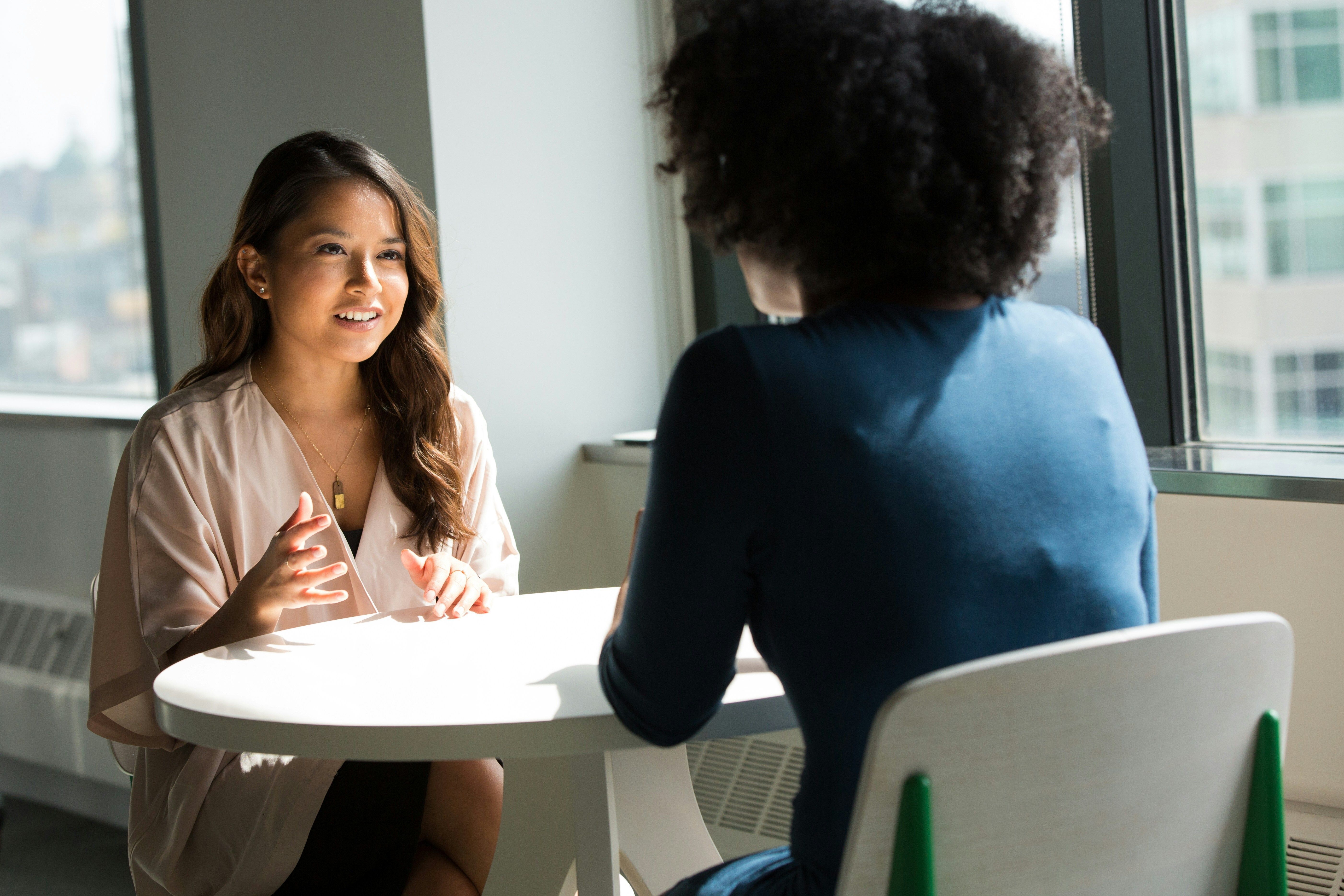 Two women sit at a table discussing business items.