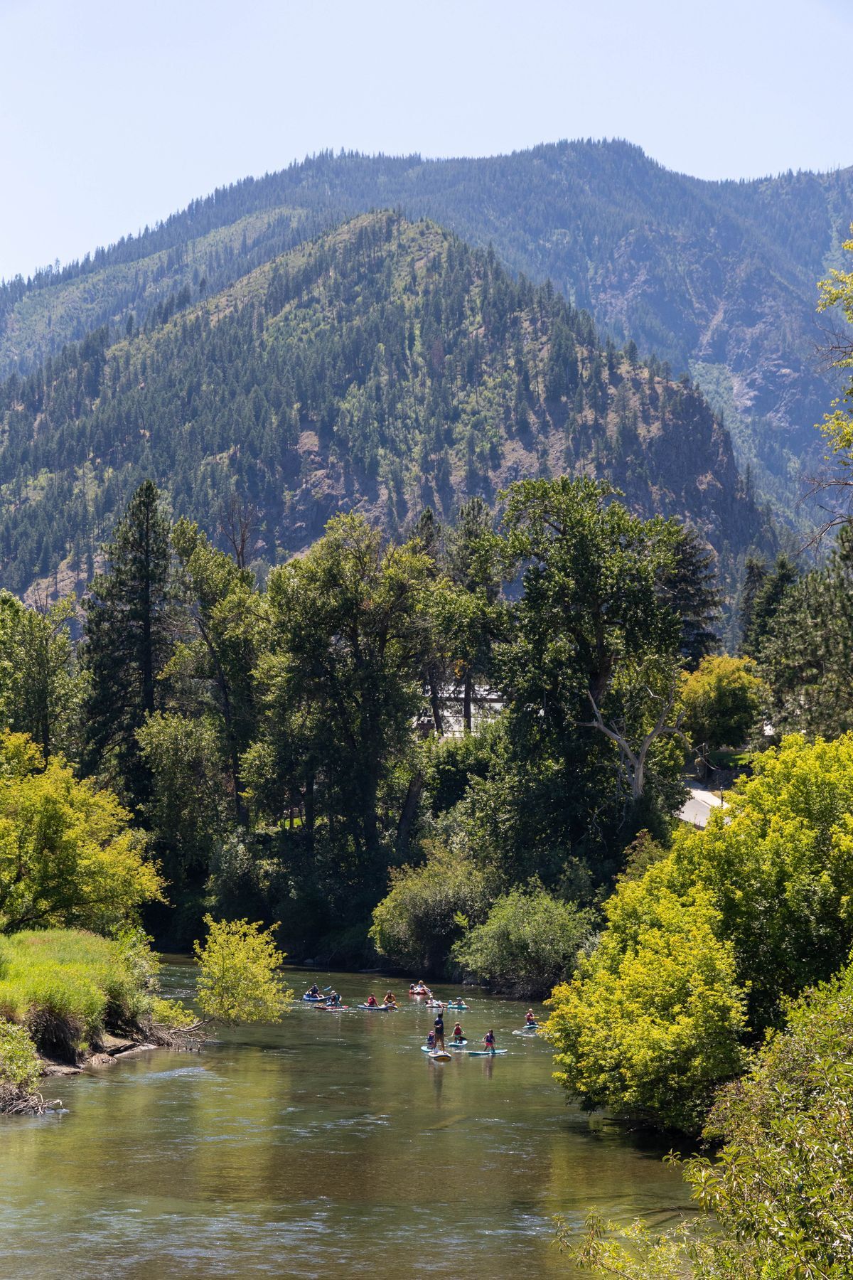 Overlooking the Wenatchee River valley with mountains, trees, and the river, with WRI campers paddling the river in the distance.