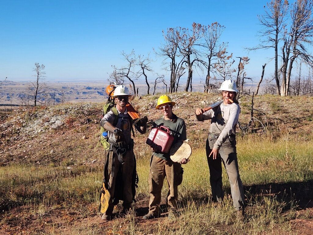 A crew member and two leaders stand on a hillside, smiling and making faces towards the camera.