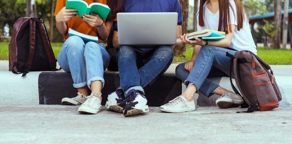 Photo of students sitting on the curb with their school supplies.