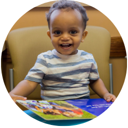 Toddler smiles with book on lap