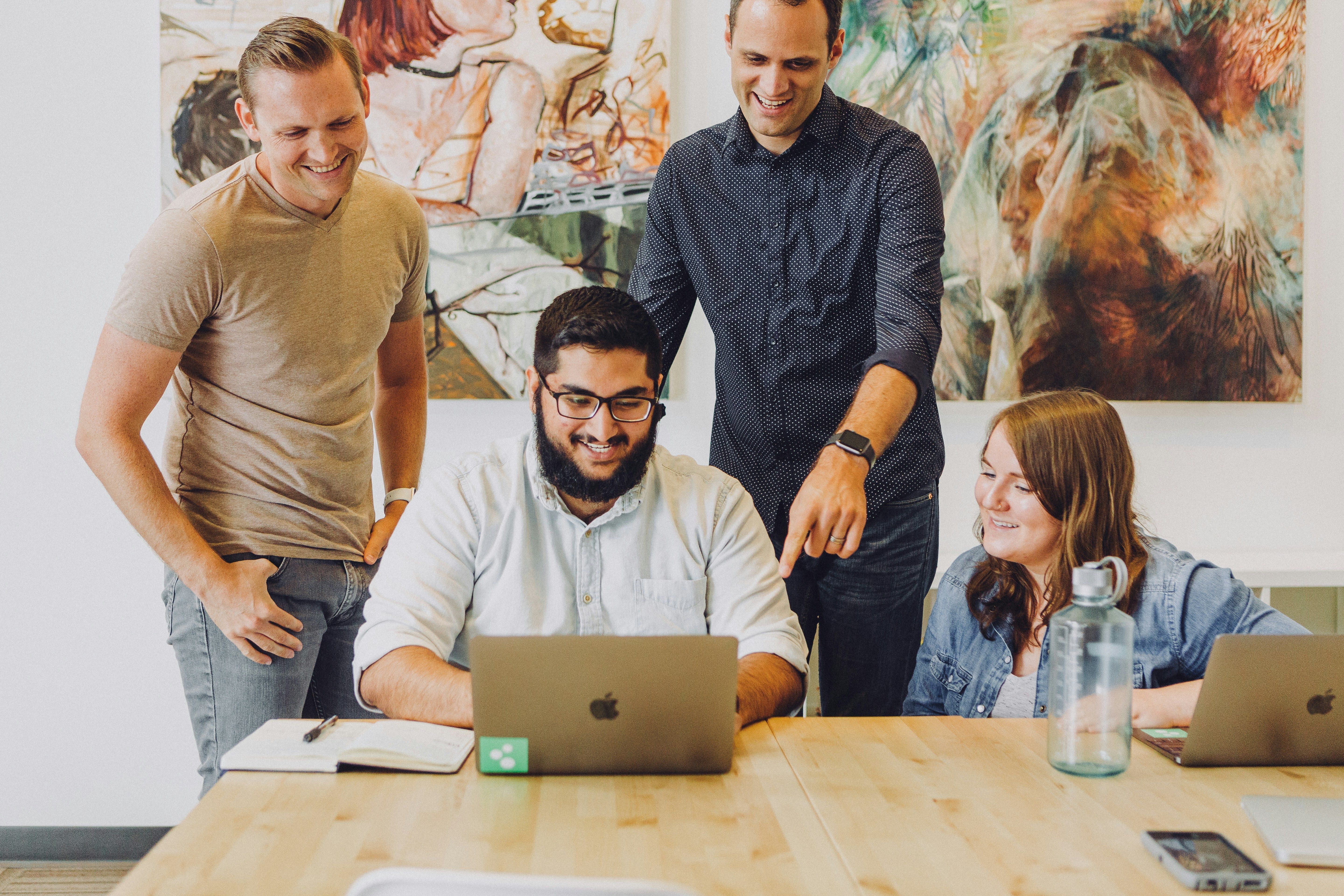 Four employees discussing information while surrounding a computer on a table.