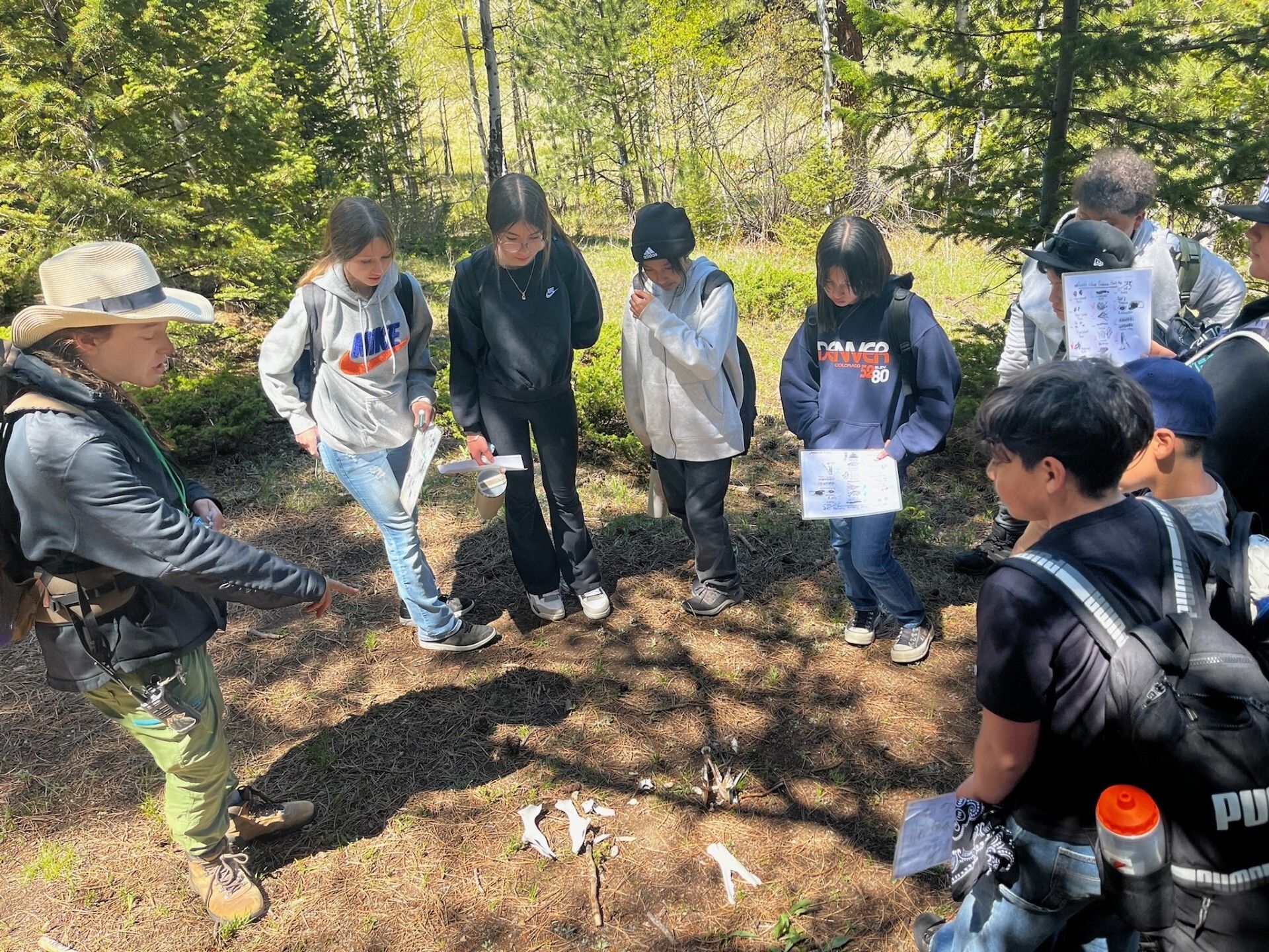 Mapleton students gathered outdoors with a guide, exploring nature and examining bones during a hands-on learning experience