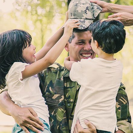 A soldier in uniform smiles while embracing two children.