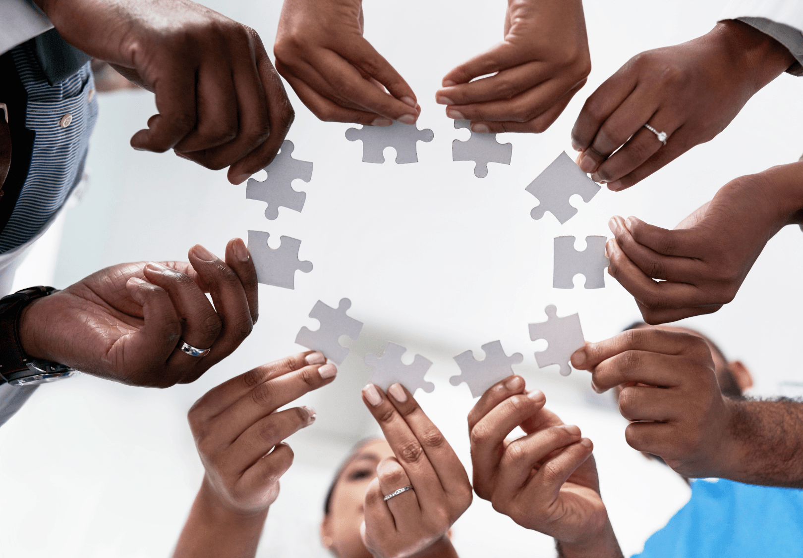Many hands of diverse skin tones holding puzzle pieces, symbolizing teamwork and collaboration
