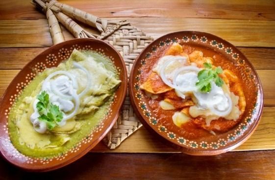 Two plates of enchiladas topped with cream, sliced onion and cilantro.