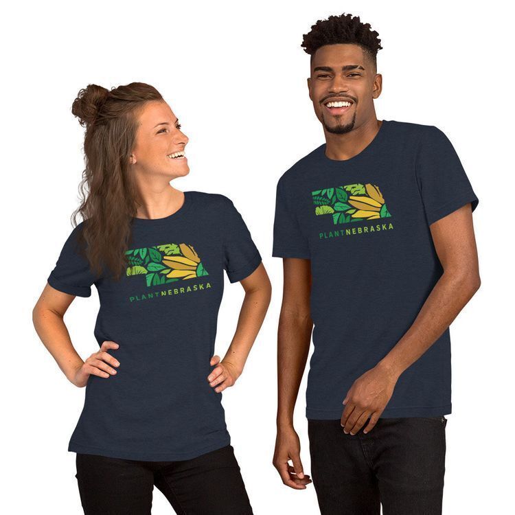 Two smiling models wearing heather navy Plant Nebraska t-shirts featuring a Nebraska state outline filled with a green and yellow leaf and sunflower design.