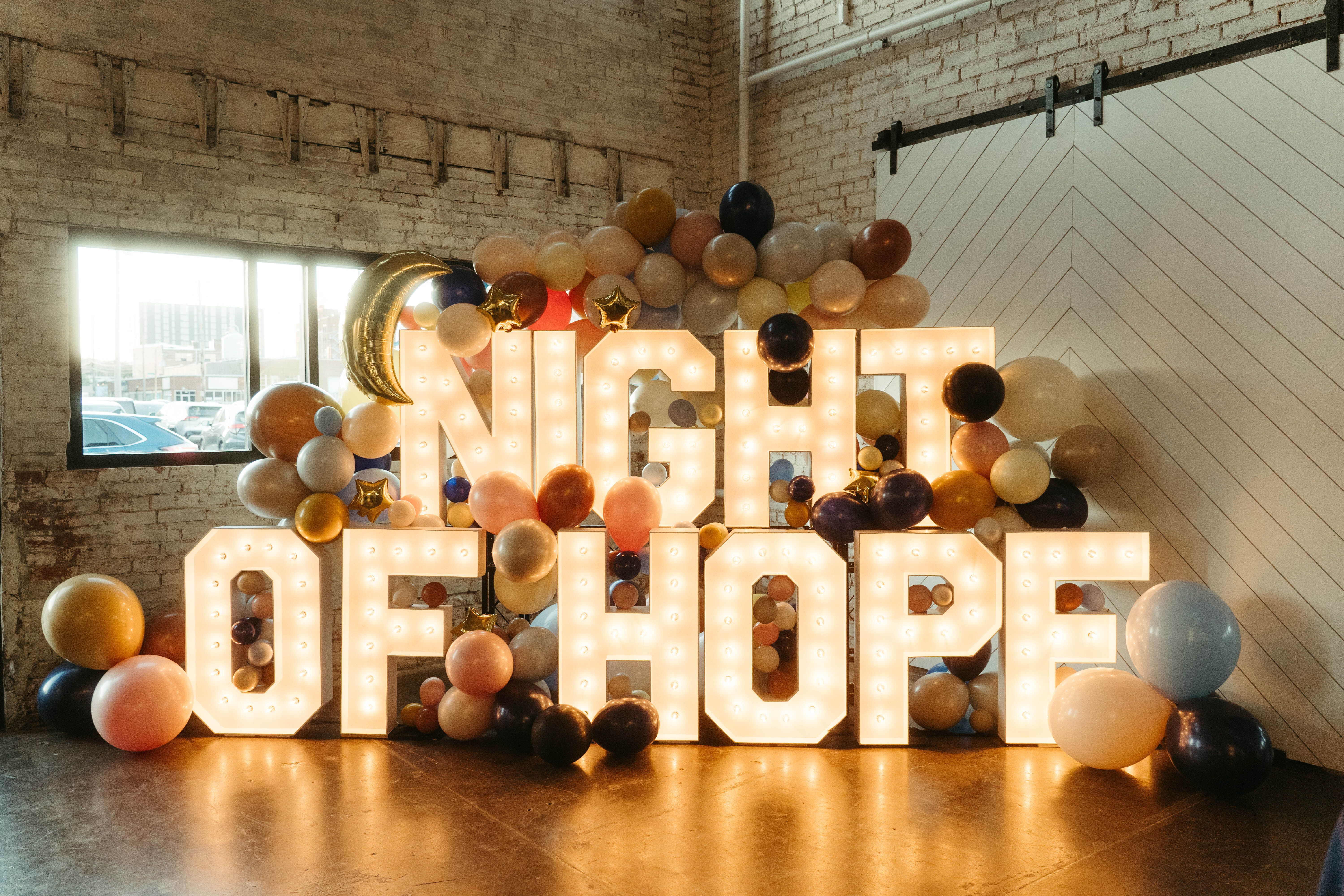 Illuminated letters spell Night of Hope surrounded by balloons