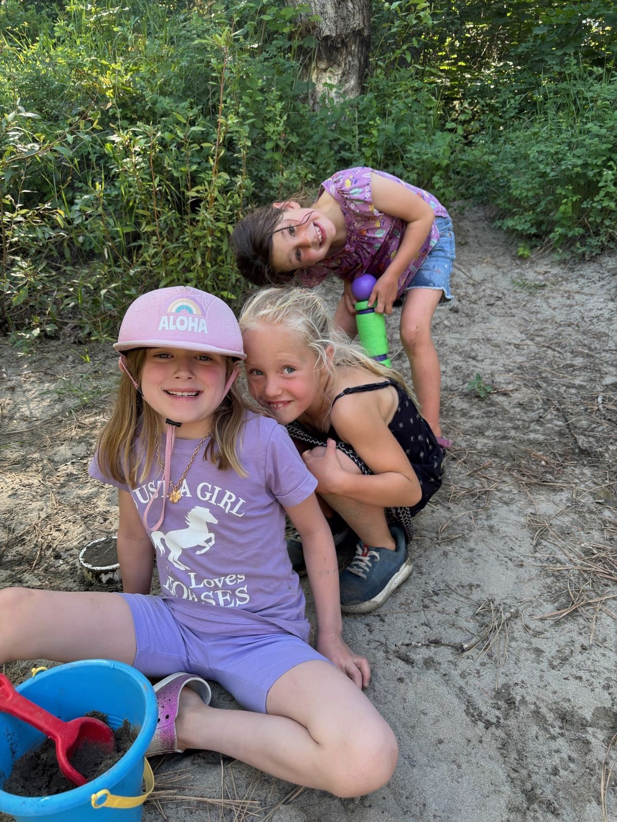 Three girls posing for the camera in the sand on Barn Beach making sand sculptures.