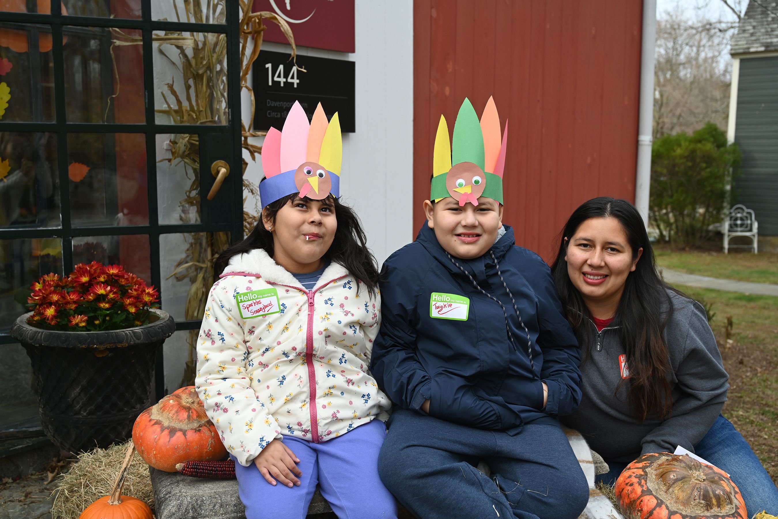 Family of three posts in front of the Circle of Care office showing off their turkey headband crafts
