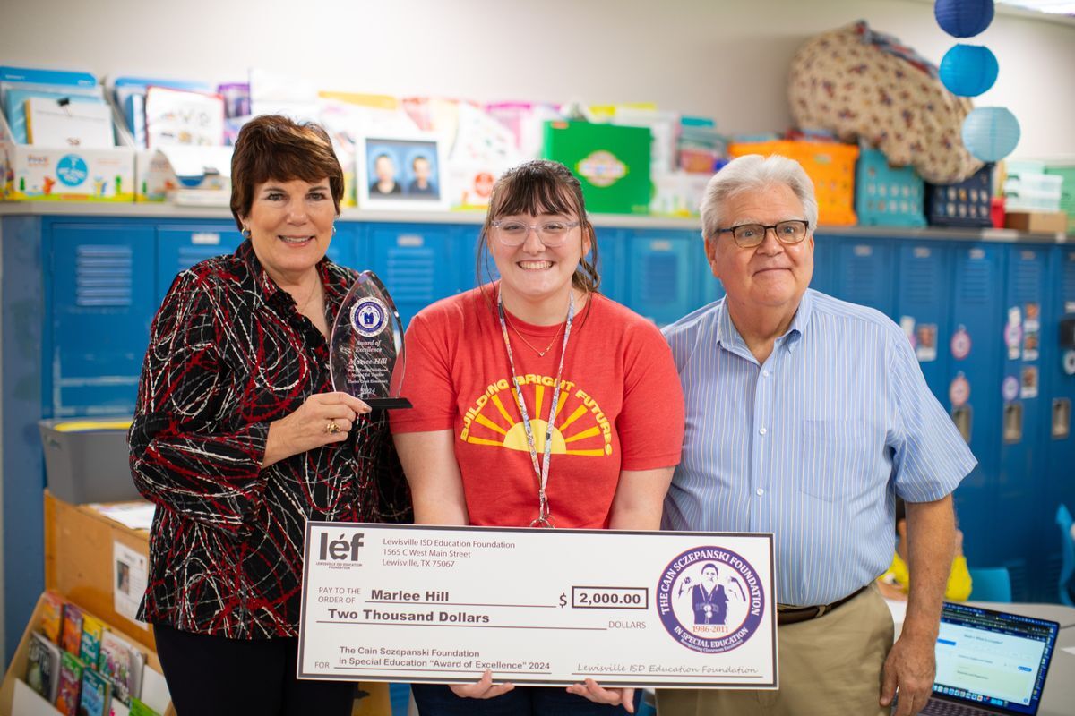 A teacher grins in excitement holding her big presentation check and smiles with the Sczepanski family