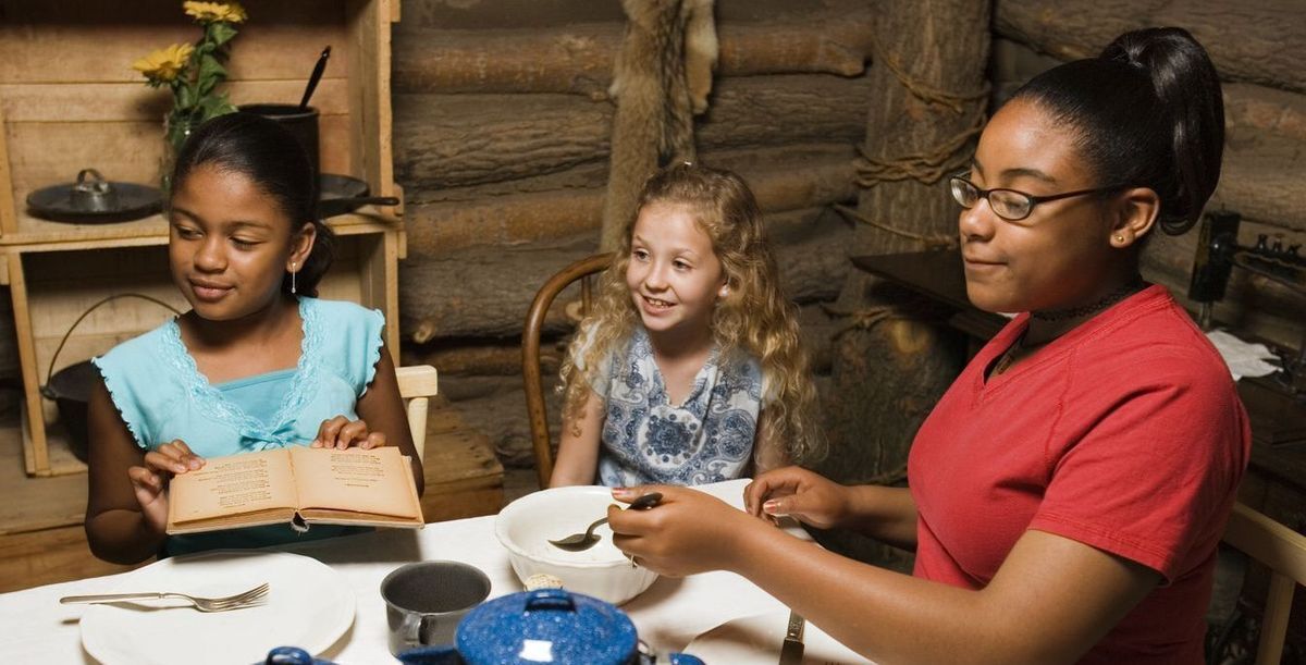 Three girls seated at a table playing house in the Smoky Hill Museum's dugout home exhibit