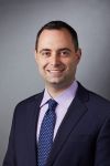 Photo of Dr. David Assis wearing a blue tie and suit, smiling at the camera