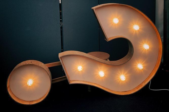 Photograph of a lit up marquise question mark sign on its side.