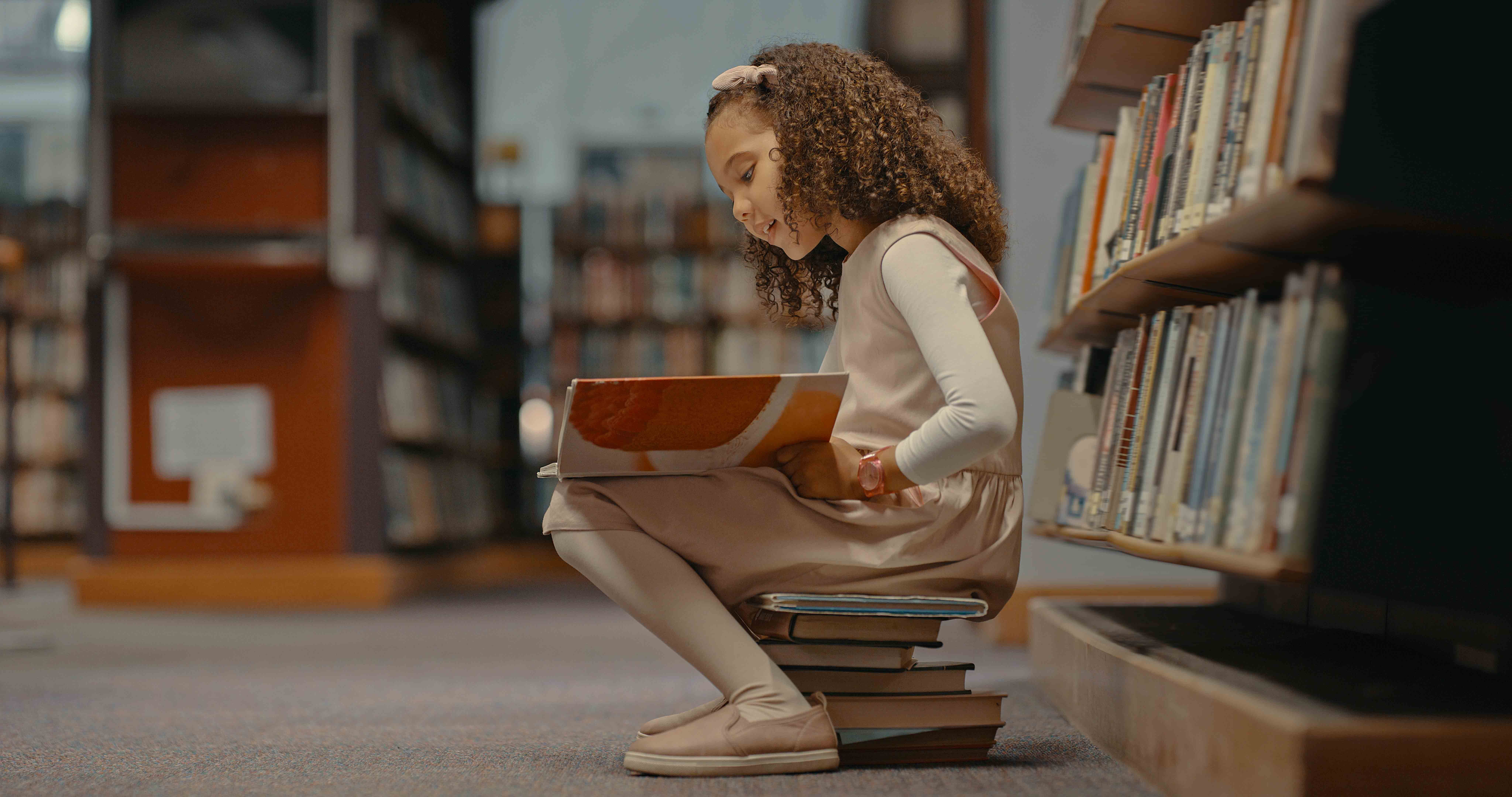 Child reading while sitting on books at the library