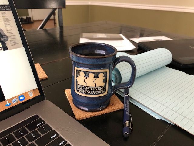 A table with a lap top, blue PSC Partners mug, a pen, and a pad of lined paper
