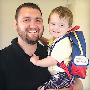 A father of a child with Down syndrome carries his son with his school backpack.