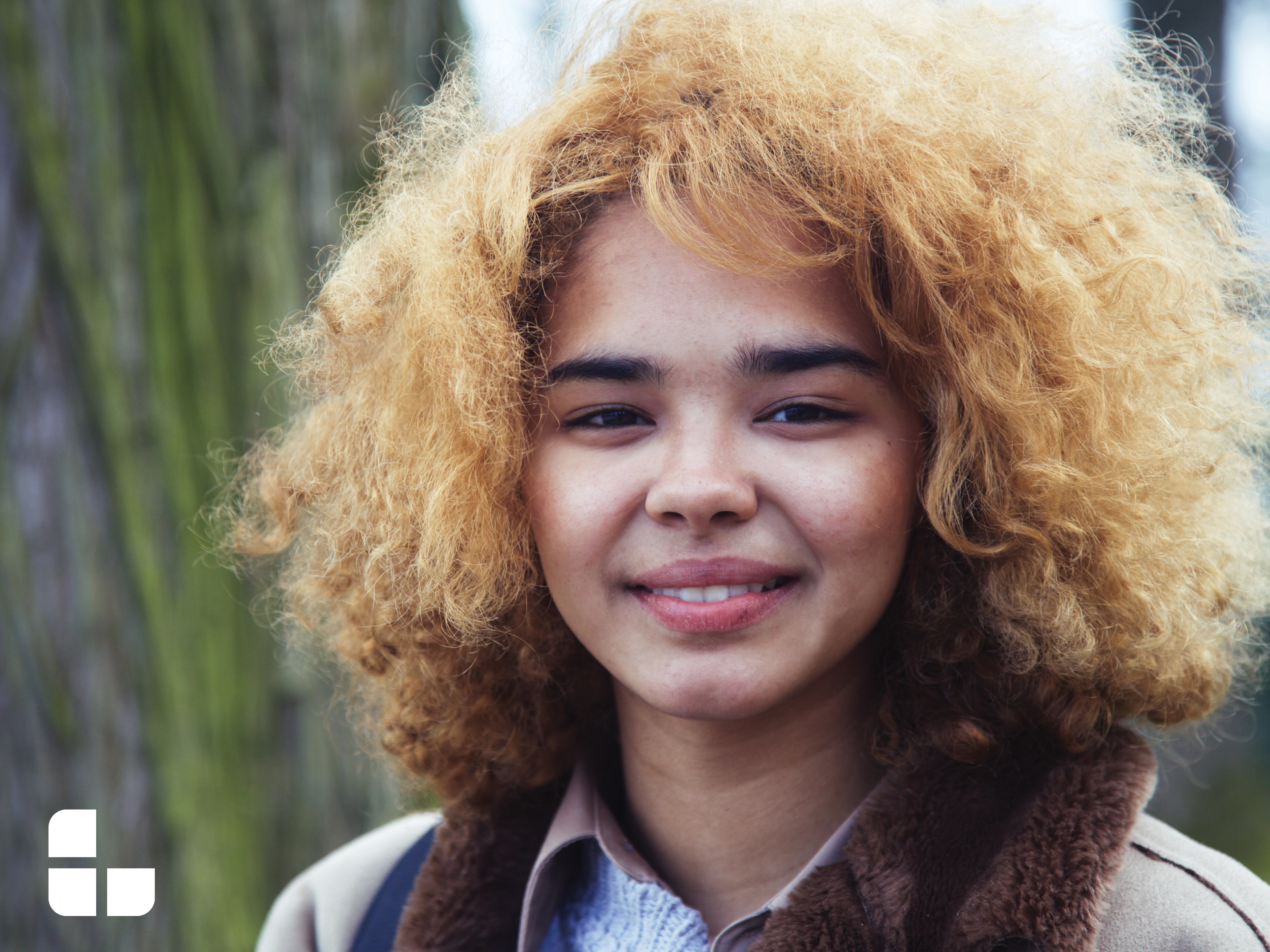 A picture of a girl with very curly blond hair and a beige jacket.