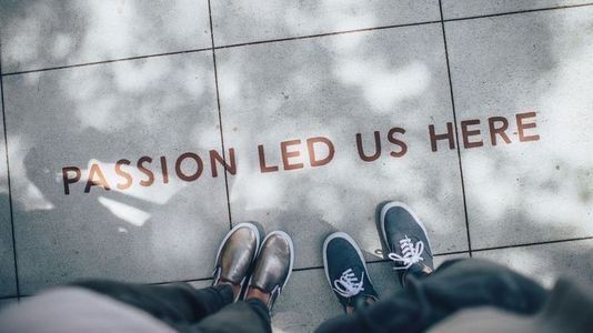 two people looking down at the sidewalk where the words "passion led us here" are written