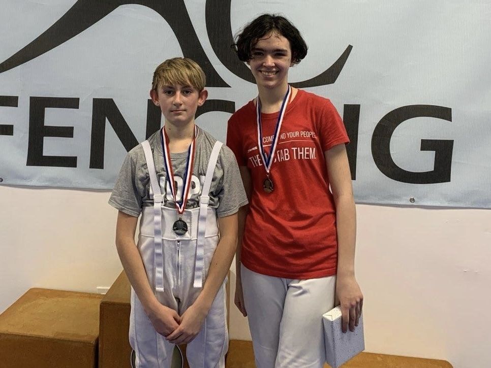 Two youth fencers with medals smile for the camera